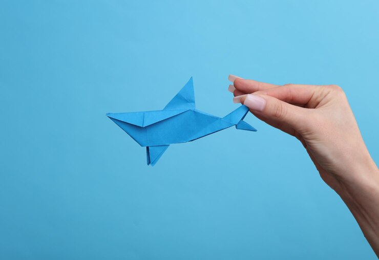 Foto la mano de la mujer sostiene un tiburón origami sobre un fondo azul hobby creatividad