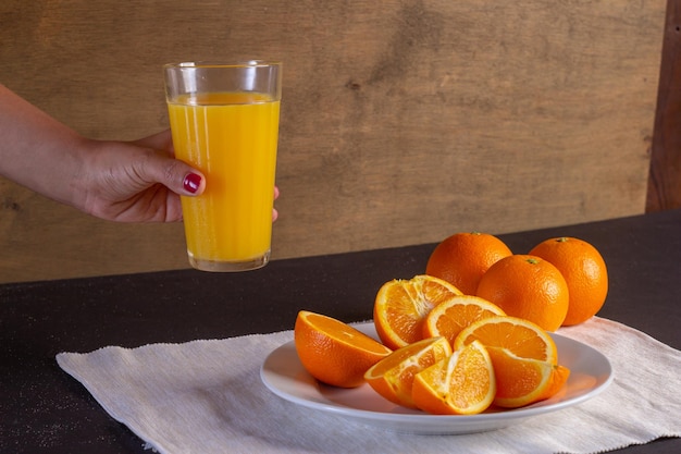 Mano de mujer sostiene un vaso de jugo en una mesa, Fondo de fruta de naranja saludable muchas frutas frescas de naranja, vida sana.