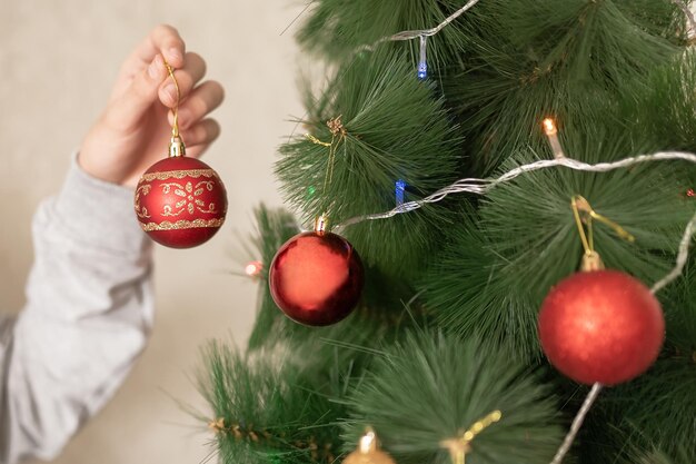 Foto la mano de una mujer con un suéter cuelga una bola roja en el árbol de navidad.