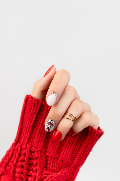 Mano de mujer en suéter con manicura roja sobre gris