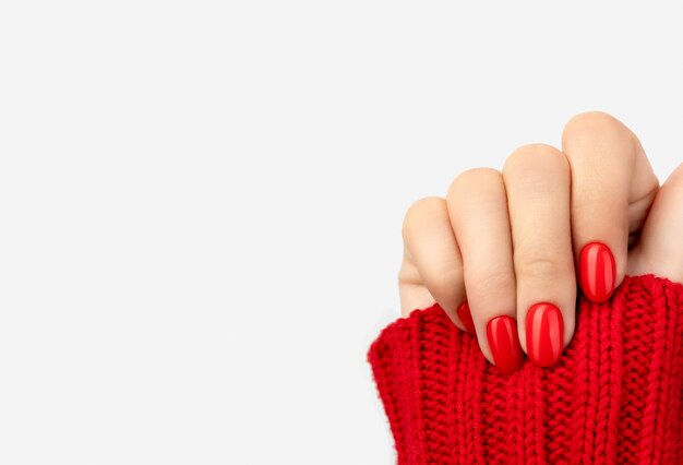 Mano de mujer en suéter con manicura rojo sobre gris