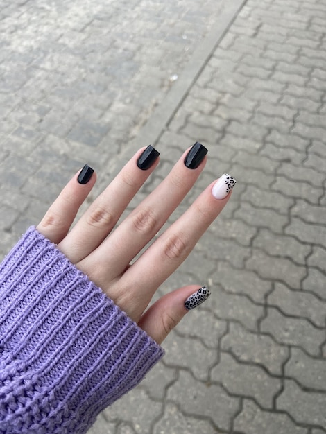 La mano de una mujer con un suéter morado y un esmalte de uñas en blanco y negro.
