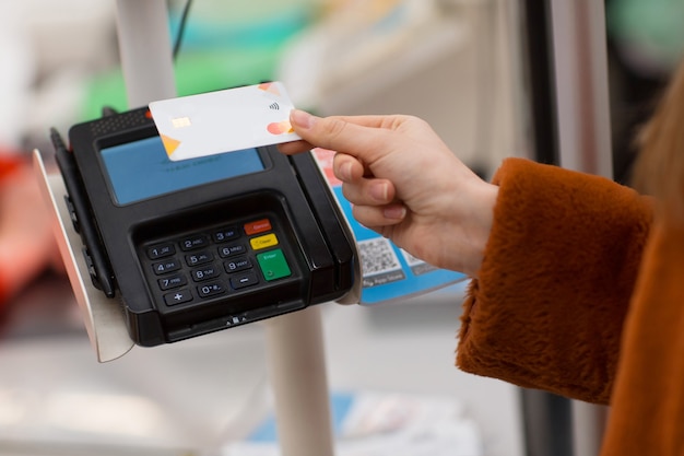 Mano de mujer con tarjeta bancaria de crédito paga las compras en el mostrador de la caja en el pago sin contacto de la tienda en nuevas compras normales