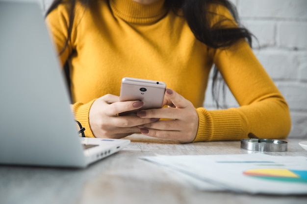 Mano de mujer teléfono inteligente con computadora en la mesa de oficina