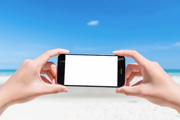 mano de mujer con teléfono inteligente en la playa.