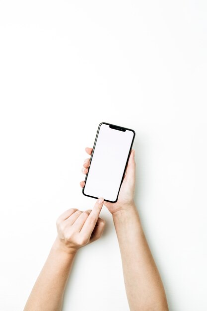 Mano de mujer tocando la pantalla del teléfono inteligente en blanco. vista superior