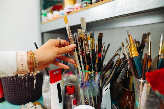 Mano de mujer toma un pincel de un soporte para herramientas de pintura Mano de mujer y un pincel para pintar