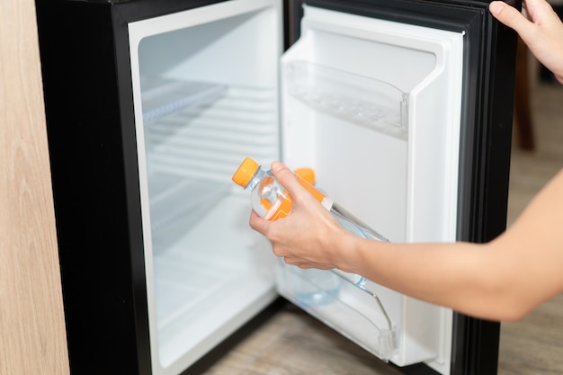 Mano de mujer tomando la botella de agua del refrigerador.