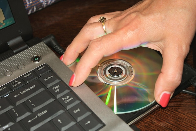 Foto mano de mujer tomando un disco dvd de una computadora portátil