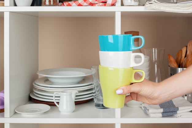 Mano de mujer tomando piezas de vajilla del estante en la cocina