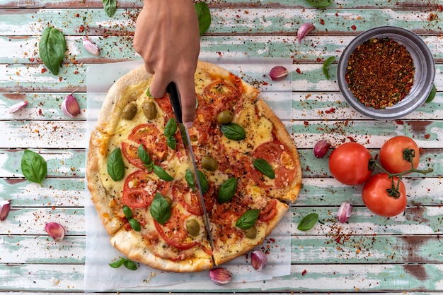 Mano de una mujer tomando una rebanada de pizza visto desde arriba en tableros turquesa rústico