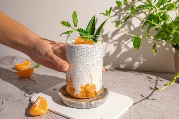 La mano de la mujer tomando un vaso con pudín de chía y mandarinas