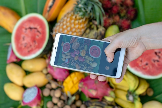 Foto mano de mujer tomar fotografía telefónica de frutas tropicales foto de teléfono inteligente del desayuno dulce mango papaya pitahaya plátano sandía piña raw vegano vegetariano comida saludable