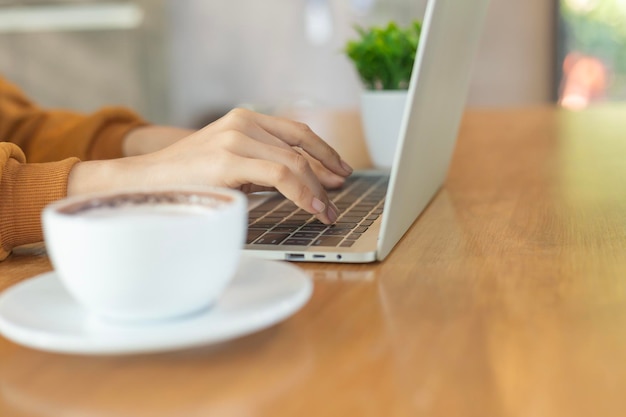 La mano de la mujer trabajando y escribiendo en el teclado del portátil en una mesa de madera