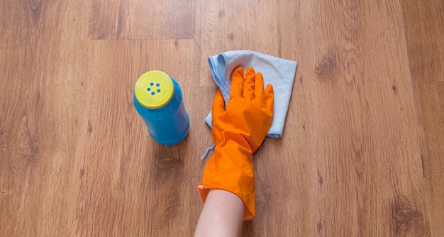 Una mano de mujer con trapos azules limpia el piso de madera
