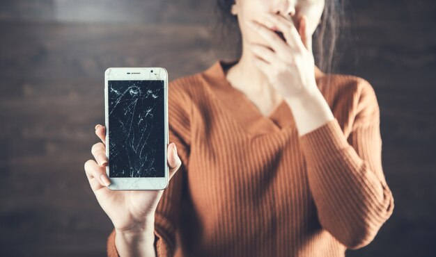 Mano de mujer triste roto teléfono inteligente en la oscuridad