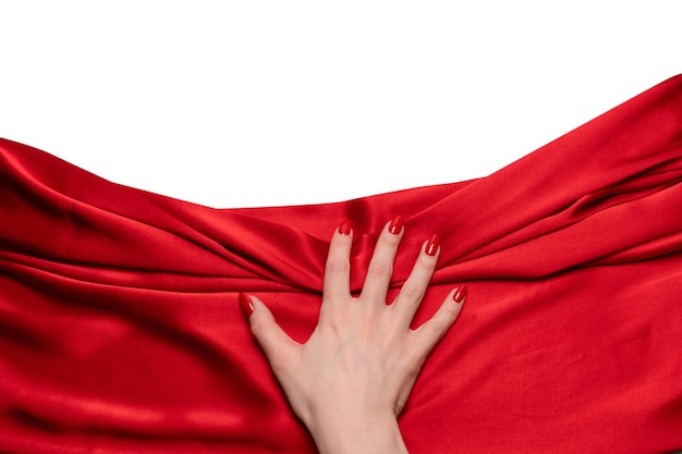 La mano de una mujer con uñas rojas está tratando de arrancar una tela de seda roja.