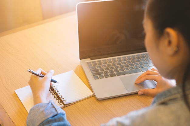 La mano de la mujer usando la computadora portátil y escribiendo en libreta.