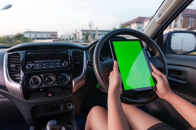 Mano de mujer usando tableta con monitor de pantalla verde en blanco en automóvil SUV