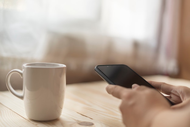 Mano de mujer usando un teléfono inteligente en el escritorio con una taza de café