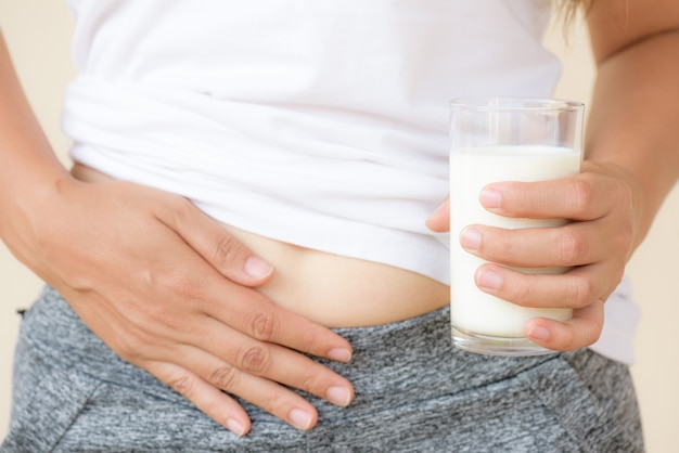 Mano de mujer con vaso de leche que tiene mal dolor de estómago debido a la intolerancia a la lactosa.