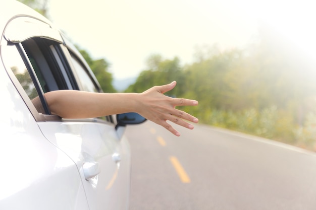 Mano de mujer en la ventana del coche en un camino rural