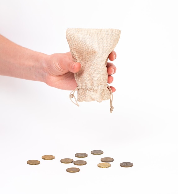 Foto la mano de una mujer vierte los restos de monedas de una bolsa de lona en un primer plano de fondo blanco