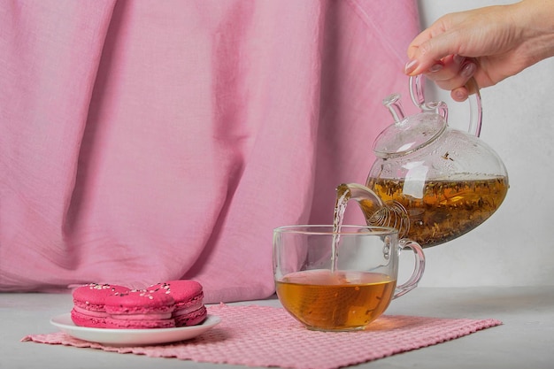 La mano de la mujer vierte té de hierbas en una taza de postre