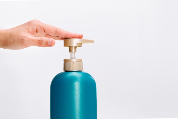 La mano de las mujeres aplica la botella del acondicionador del champú del pelo en el fondo blanco.