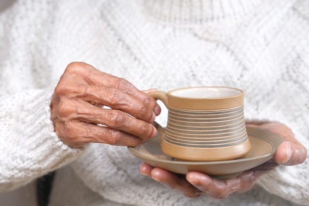 Mano de mujeres mayores sosteniendo una taza de té verde