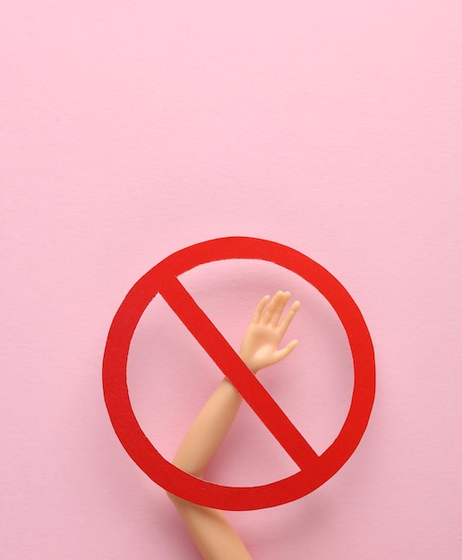 Mano de muñeca con señal de prohibición en fondo rosa
