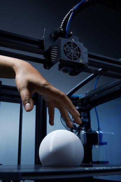 Una mano neutra en cuanto al género que se extiende hacia un objeto blanco redondo impreso en 3D hecho de plástico reciclado para recoger el concepto futurista de nuevas posibilidades de trabajo para las pequeñas empresas mediante la impresión en 3D de una foto Jpg