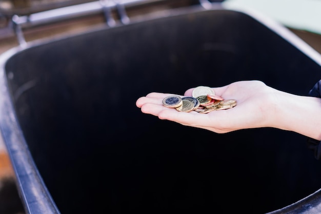 La mano de una niña arroja monedas de euro a un basurero tirado en la calle