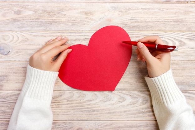 Mano de niña escribiendo la carta de amor el día de san valentín Postal hecha a mano de corazón rojo.