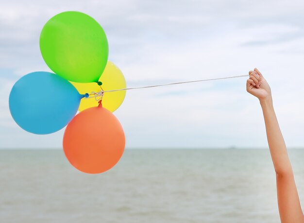 Mano de niña con globos de colores en la playa