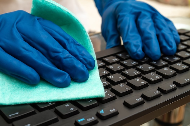 La mano de la niña en un guante protector azul limpia el teclado con un paño