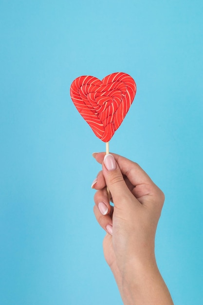 La mano de una niña con un hermoso caramelo en forma de corazón sobre un fondo azul.