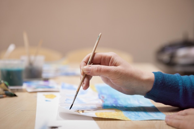 Mano de niña con pincel pintando con acuarelas. Autodesarrollo y aficiones. Enfoque selectivo.