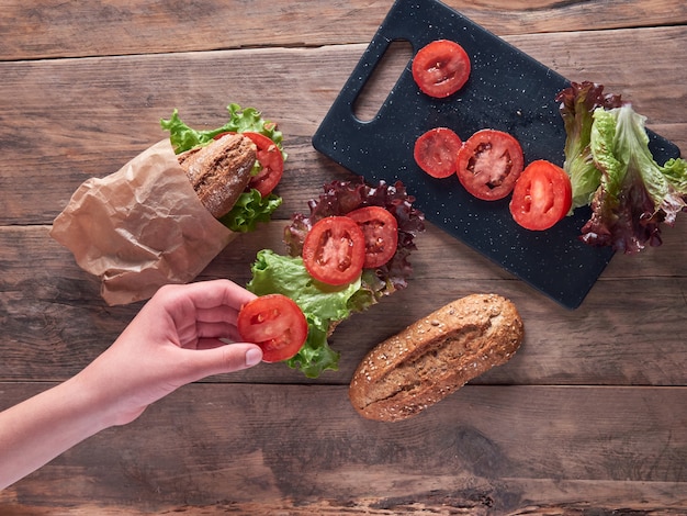 Mano de una niña preparando un sándwich de baguette de tomates y lechuga