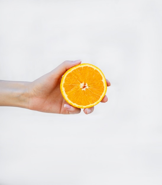 La mano de la niña sostiene la mitad de una naranja jugosa en blanco