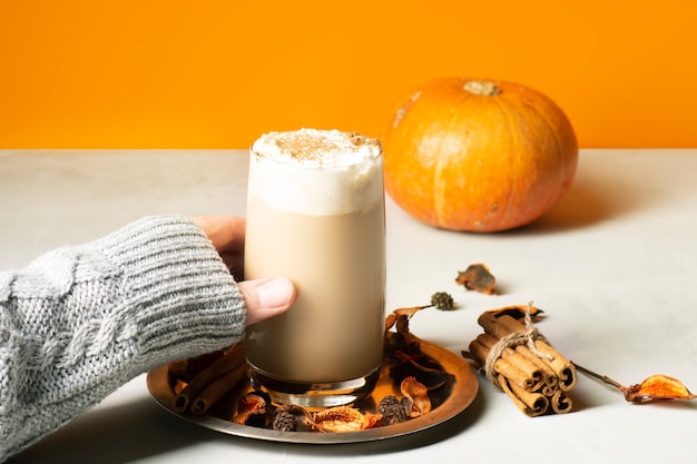 La mano de la niña con un suéter gris toma un café con leche de especias de calabaza en un vaso