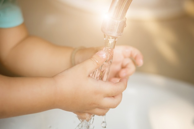 Mano de niño abierta para beber agua del grifo.