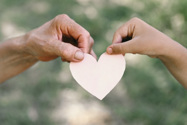 La mano del niño y la abuela de la mano vieja sostienen el corazón. Concepto de idea de amor familiar protegiendo a niños y ancianos abuela amistad unión