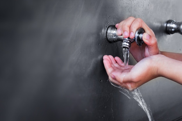 Mano del niño con agua potable que sale del agua del grifo