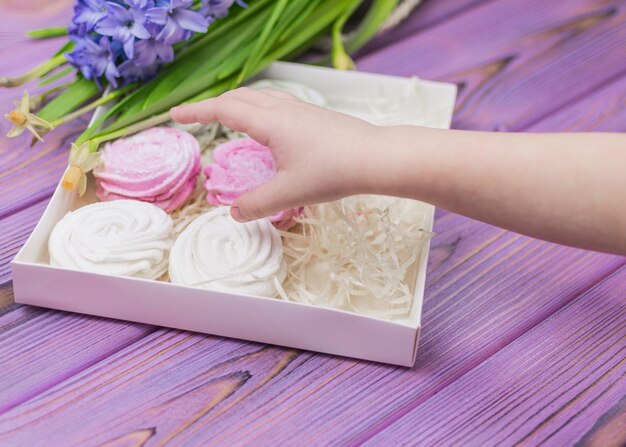 La mano del niño busca una caja de dulces con un céfiro de malvavisco