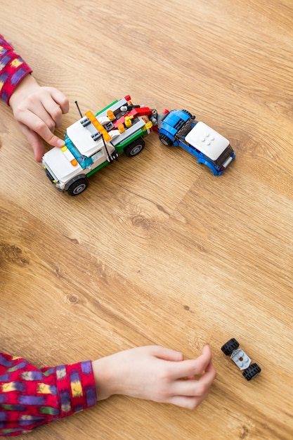 Mano de niño con coches de juguete. Niño jugando en un piso de madera. Éste debe ser reparado. El conductor necesita ayuda de inmediato.