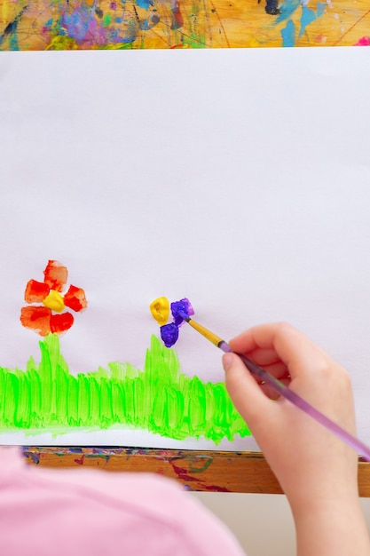 Mano del niño dibujando flores en una hoja de papel blanca sobre un caballete. Concepto del día de la tierra y los niños.