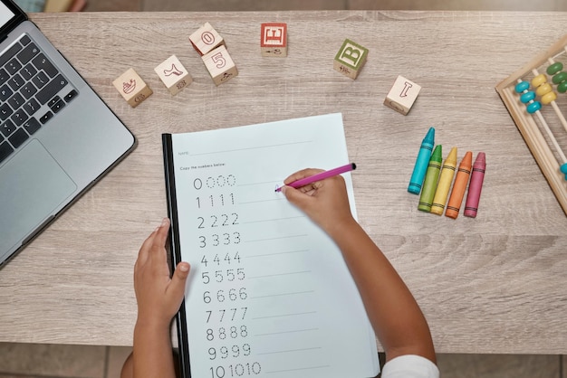 Mano del niño y escritura de tareas matemáticas y desarrollo para el crecimiento y el conocimiento en la mesa en casa desde arriba Estudiante niño y educación en línea o maestro de aprendizaje electrónico enseñando con computadora portátil y crayones