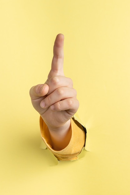 La mano del niño muestra el dedo índice hacia arriba a través del agujero en papel amarillo con el concepto de bordes rasgados, presione el botón primero