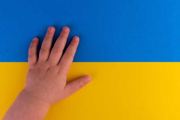 la mano de un niño pequeño en el fondo de la bandera de Ucrania